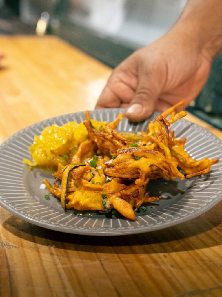 Fritura de verduras en un plato gris, sujeto por una mano del equipo de Condendê